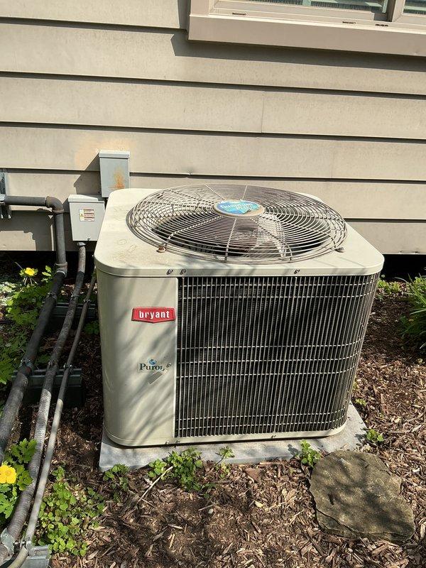 Completed comprehensive gold-level air conditioning inspection on a 10+ year old Bryant condensing unit located on exterior concrete pad with air handler/coil in basement. System currently operational at time of assessment. Documented equipment condition through photographic inspection showing condenser unit with proper clearances, secure refrigerant line connections, and adequate airflow access. Provided estimate for complete HVAC system replacement based on equipment age and homeowner consultation.