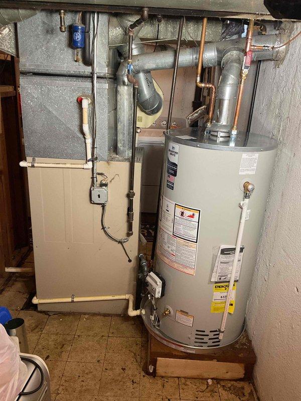 Completed installation of a 50-gallon tanked water heater in residential basement utility room. Unit was properly positioned on wooden platform with metallic drip pan, connected to existing gas line via flexible CSST connector, and vented through existing vent system. All plumbing connections, electrical controls, and safety devices were installed and reconnected per manufacturer specifications and local code requirements.