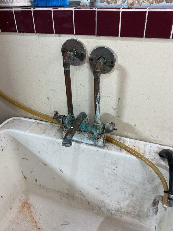 Replaced corroded laundry tub faucet assembly with new basic faucet and shutoff valves. Removed existing copper pipe connections showing extensive green patina and verdigris corrosion on brass fittings and valve mechanisms. Installed new wall-mounted faucet assembly with proper supply line connections to existing copper stub-outs.