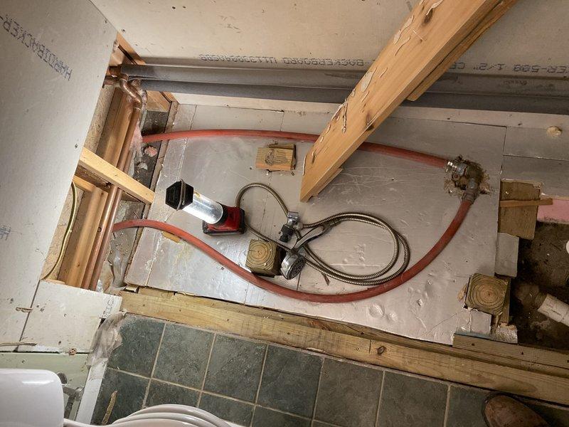Performed diagnostic assessment and initial work on shower plumbing relocation project in bathroom undergoing renovation. Accessed subfloor cavity through exposed framing to evaluate existing water supply lines and drainage piping configuration. Identified routing path for relocating shower supply lines from current under-fixture location to alternate position as requested. Installed flexible PEX supply lines with appropriate securing blocks and mounting points on cement board underlayment. Positioned water supply connections and valve assembly for future fixture installation. Utilized vacuum equipment for debris removal and maintained clean work area throughout process. Project documented as potentially requiring additional scope determination pending full assessment of structural and plumbing requirements for complete relocation.