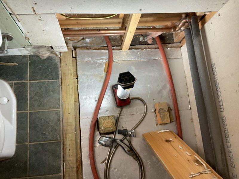 Performed diagnostic assessment and initial work on shower plumbing relocation project in bathroom undergoing renovation. Accessed subfloor cavity through exposed framing to evaluate existing water supply lines and drainage piping configuration. Identified routing path for relocating shower supply lines from current under-fixture location to alternate position as requested. Installed flexible PEX supply lines with appropriate securing blocks and mounting points on cement board underlayment. Positioned water supply connections and valve assembly for future fixture installation. Utilized vacuum equipment for debris removal and maintained clean work area throughout process. Project documented as potentially requiring additional scope determination pending full assessment of structural and plumbing requirements for complete relocation.