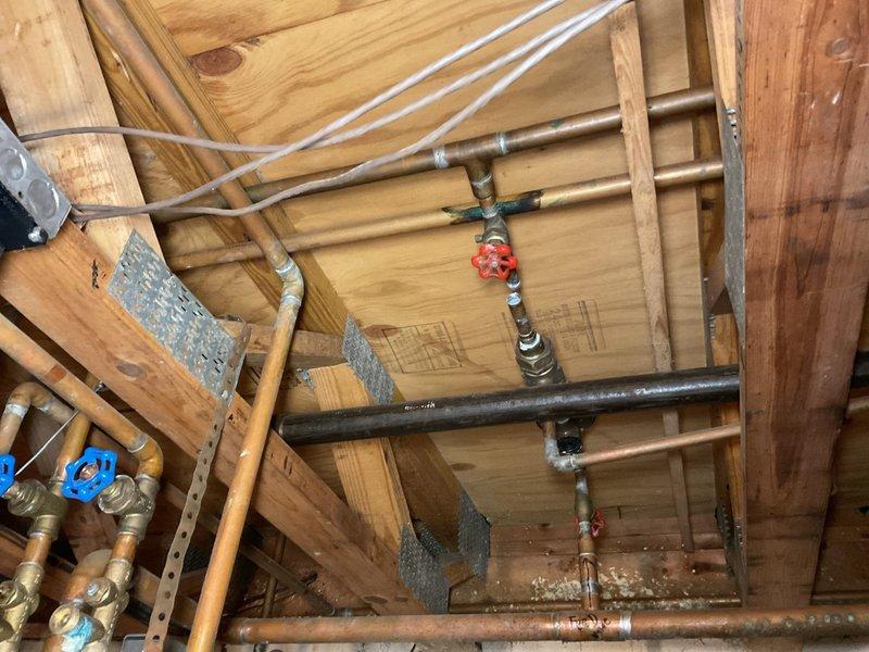 Responded to service call for complete copper piping replacement in residential basement following theft of existing plumbing infrastructure. Conducted thorough assessment of remaining plumbing systems, including inspection of ceiling-mounted pipe runs, existing PVC drainage lines, and connection points. Documented current conditions showing exposed joists, partial copper piping with brass valves, red-handled shutoff valve, and white PVC sections requiring integration with new copper installation. Evaluated bathroom fixture connections including toilet, vanity sink with chrome faucet, and associated supply lines to determine scope of repiping required. Photographed existing plumbing configuration, valve locations, pipe routing through floor joists, and fixture rough-in points to develop comprehensive estimate for new copper piping system installation throughout basement and bathroom areas.