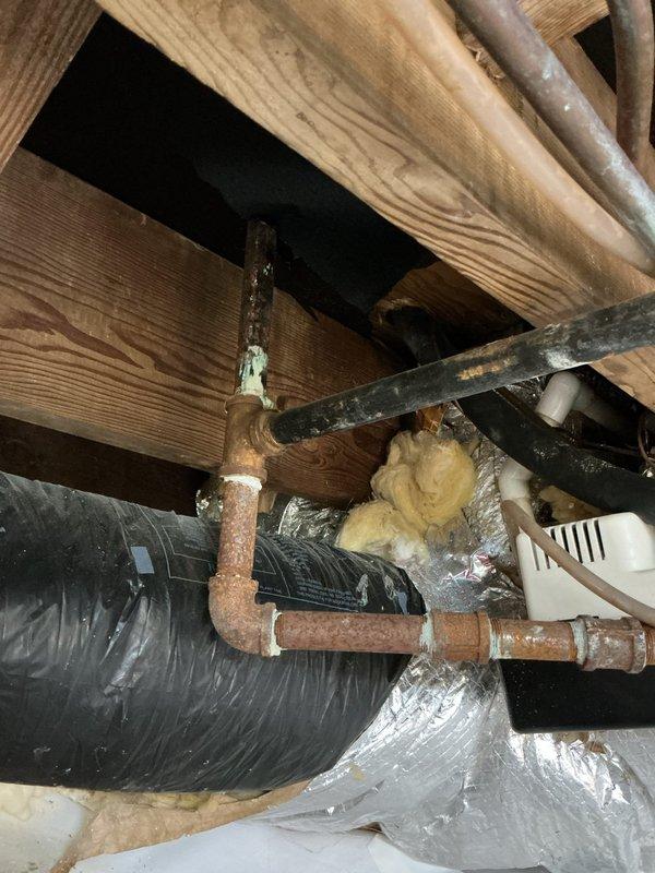 Completed comprehensive plumbing estimate for relocating supply and drain lines to opposite side of wall, along with repositioning water heater and hot water meter in 1950s-era residential property. Assessed existing copper supply piping showing significant age-related corrosion, oxidation, and green patina buildup throughout crawl space, along with galvanized steel drain lines and PVC trap assembly in basement utility area. Documented current plumbing infrastructure including corroded copper pipes with various fittings and joints secured to wooden joists, existing drain configuration with trap and shutoff valves, and water heater currently located in mudroom requiring relocation.

Evaluated scope of work necessary to reroute hot and cold water supply lines from current location through wall cavity to new position, including removal of deteriorated copper piping and installation of new supply lines. Assessed requirements for relocating drain lines including proper venting and trap conf