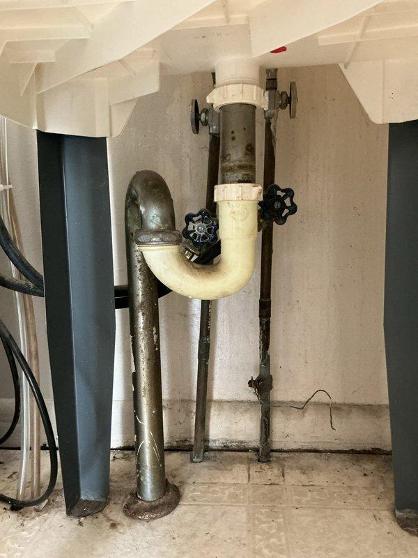 Completed comprehensive plumbing estimate for relocating supply and drain lines to opposite side of wall, along with repositioning water heater and hot water meter in 1950s-era residential property. Assessed existing copper supply piping showing significant age-related corrosion, oxidation, and green patina buildup throughout crawl space, along with galvanized steel drain lines and PVC trap assembly in basement utility area. Documented current plumbing infrastructure including corroded copper pipes with various fittings and joints secured to wooden joists, existing drain configuration with trap and shutoff valves, and water heater currently located in mudroom requiring relocation.

Evaluated scope of work necessary to reroute hot and cold water supply lines from current location through wall cavity to new position, including removal of deteriorated copper piping and installation of new supply lines. Assessed requirements for relocating drain lines including proper venting and trap conf