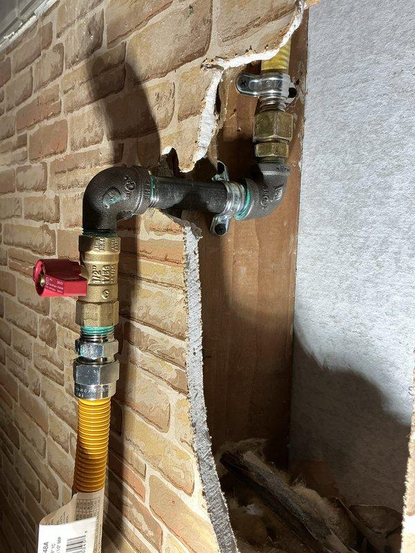 Responded to gas line repair estimate request and performed thorough inspection of existing gas line installation serving fireplace unit. Documented current configuration including brass shut-off valve with red handle, corrugated stainless steel tubing (CSST) connection, and associated fittings at wall penetration point between brick and drywall surfaces. Evaluated gas line routing from supply point through wall assembly to fireplace appliance, noting flexible gas connector installation and valve accessibility. Captured detailed photographs of gas piping components, connections, and fireplace interior to support repair estimate development and identify scope of work required for code-compliant gas line modifications or replacement.