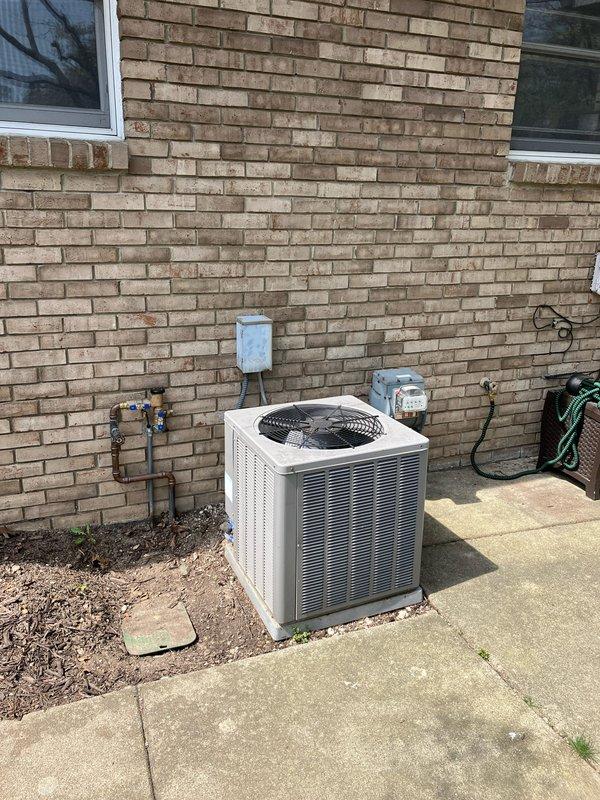 Provided estimate for replacement of aging outdoor AC condenser unit located on exterior concrete pad alongside building. Existing unit is operational but over 10 years old, with associated basement furnace equipment running on natural gas. Documented current system configuration including refrigerant lines, electrical disconnect, and utility connections for replacement specifications.