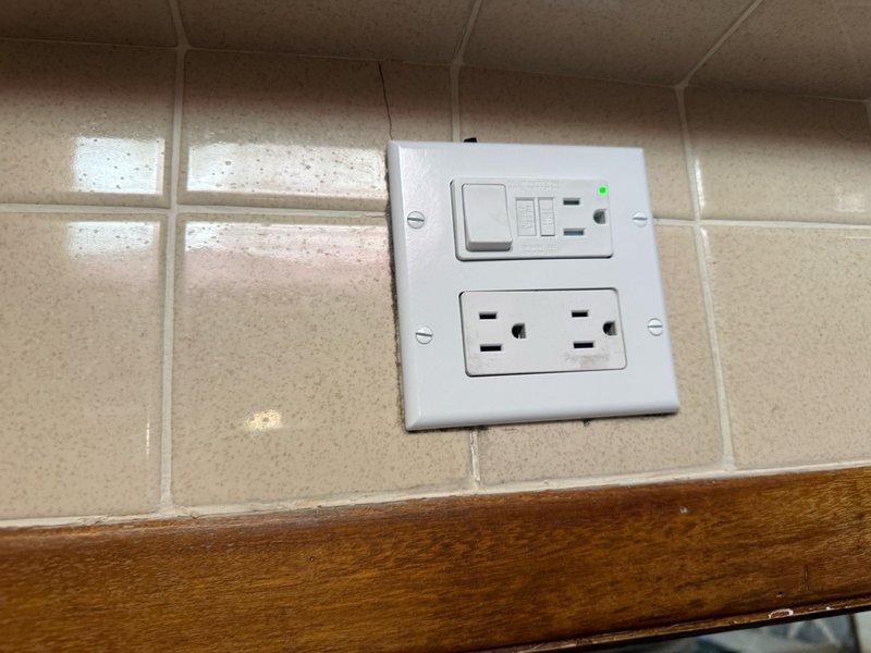 Installed bathroom exhaust fan in bedroom-adjacent bathroom area with proper ventilation routing. Upgraded electrical system to include GFCI-protected outlet with integrated switch for fan control, plus additional standard duplex receptacle on tiled bathroom wall. Work included running new electrical circuit, mounting ventilation grille, and ensuring all components meet current electrical code requirements for bathroom moisture protection.