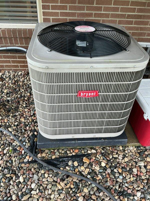 Completed comprehensive Gold AC Inspection on 2016 Bryant outdoor condenser unit and basement-located air handler system. System confirmed operational with condenser positioned on proper pad foundation with adequate clearance, decorative rock surround maintained clear of debris, and all exterior components including fan grille and refrigerant lines in good condition showing normal weathering consistent with unit age.