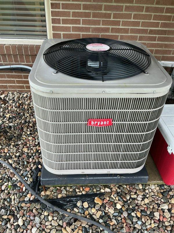 Completed comprehensive Gold AC Inspection on 2016 Bryant outdoor condenser unit and basement-located air handler system. System confirmed operational with condenser positioned on proper pad foundation with adequate clearance, decorative rock surround maintained clear of debris, and all exterior components including fan grille and refrigerant lines in good condition showing normal weathering consistent with unit age.