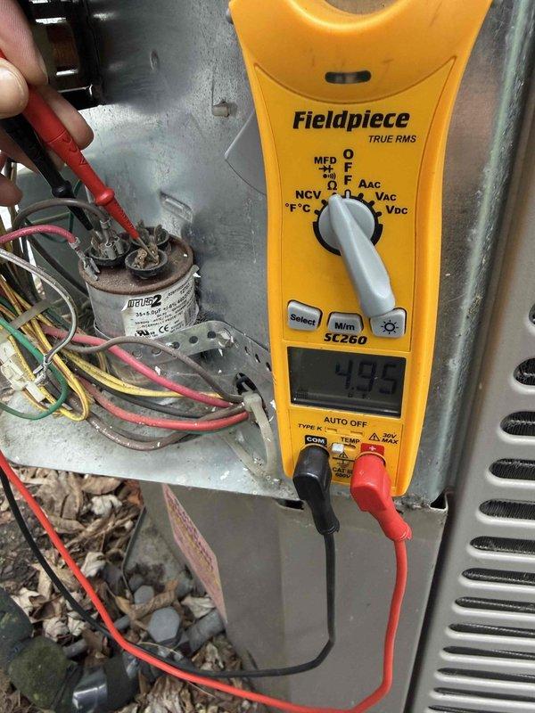 Completed comprehensive Gold AC inspection on 15-year-old residential cooling system with air handler located in basement. Performed electrical diagnostics using digital multimeter to test capacitor and measure voltage readings at outdoor condenser unit, verifying proper electrical operation of all components. Inspected outdoor condenser unit positioned on concrete pad against home exterior, checked fan assembly and grille protection, evaluated surrounding area for proper clearance and debris removal, and documented system condition through photographic records for maintenance history.