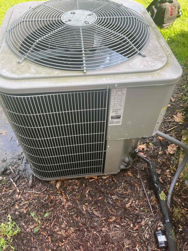 Completed comprehensive Gold AC inspection on residential 10+ year old single-zone cooling system with air handler located in basement. Performed thorough examination of outdoor condenser unit positioned on concrete pad, verifying operational status of all components including fan motor, compressor, and heat exchange coils. Inspected condenser cabinet for structural integrity, noting unit shows normal weathering consistent with age but remains in functional condition. Evaluated airflow through vertical louvers and confirmed proper clearance from surrounding vegetation and debris. Checked refrigerant lines, electrical conduit connections, and mounting stability on concrete pad. Documented equipment condition through photographic records showing condenser placement, exterior cabinet condition, and installation environment. System confirmed operational at time of inspection with no immediate service concerns identified.