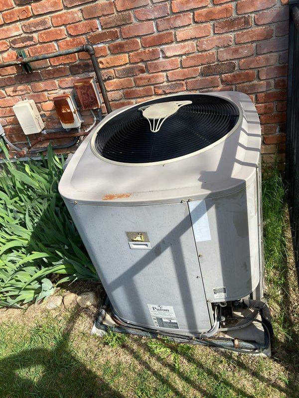 Completed comprehensive HVAC system evaluation for replacement estimate on a 2007 residential air conditioning system presenting with critically low refrigerant levels. Inspected outdoor condenser unit installed on exterior brick wall foundation and assessed basement-located air handler and evaporator coil assembly. Documented existing system age at seventeen years with noted refrigerant loss indicating potential coil leaks or compressor seal failure requiring full system replacement rather than repair. Verified furnace heat exchanger was previously replaced in 2020 and remains safe for continued operation, allowing for air conditioning replacement while retaining existing heating equipment if desired. Photographed current equipment installation including condenser placement, electrical service connections with dual meter configuration, and overall system accessibility for replacement work. Provided technical findings and replacement options to homeowner for equipment upgrade decision.