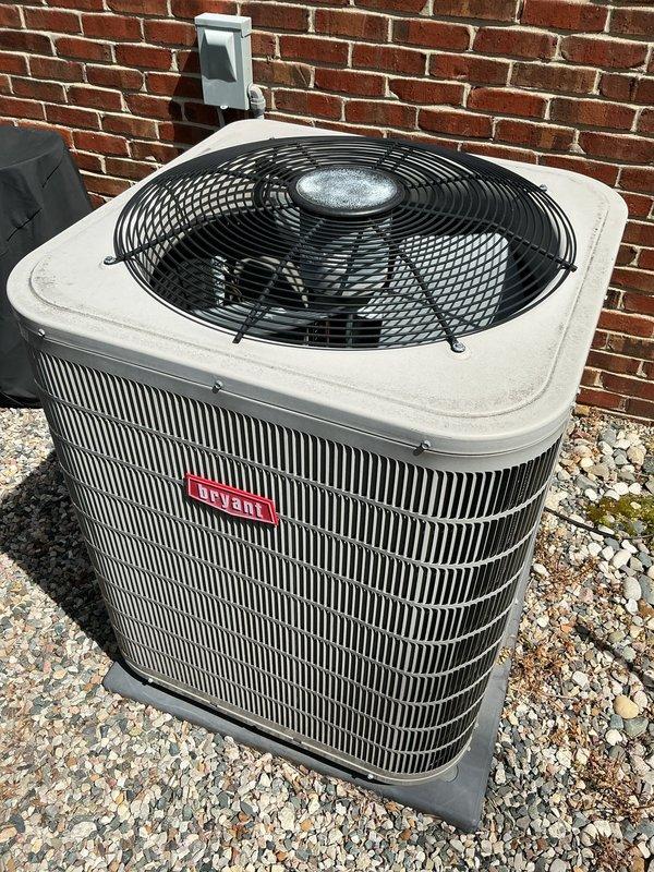 Completed comprehensive Gold AC inspection on 9-year-old Bryant residential cooling system with air handler located in basement. Unit confirmed operational at time of service. Performed thorough visual assessment of outdoor condenser unit, which is properly installed on gravel pad against exterior brick wall with appropriate electrical disconnect box mounted nearby. Condenser cabinet, fan guard, and grilles found intact with no significant damage, showing normal weathering consistent with age. Advised customer that area surrounding condenser requires clearing of debris and any animal waste to maintain proper airflow and system efficiency. All major components including fan assembly, cabinet panels, and protective guards verified to be in good working condition. Unit demonstrates proper professional installation with adequate clearance and mounting.