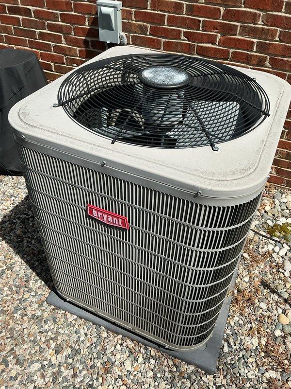 Completed comprehensive Gold AC inspection on 9-year-old Bryant residential cooling system with air handler located in basement. Unit confirmed operational at time of service. Performed thorough visual assessment of outdoor condenser unit, which is properly installed on gravel pad against exterior brick wall with appropriate electrical disconnect box mounted nearby. Condenser cabinet, fan guard, and grilles found intact with no significant damage, showing normal weathering consistent with age. Advised customer that area surrounding condenser requires clearing of debris and any animal waste to maintain proper airflow and system efficiency. All major components including fan assembly, cabinet panels, and protective guards verified to be in good working condition. Unit demonstrates proper professional installation with adequate clearance and mounting.
