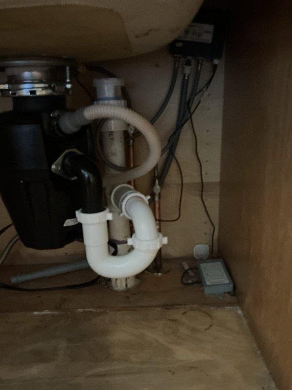 Completed kitchen sink plumbing repair involving the garbage disposal drain assembly and P-trap system beneath the cabinet. Inspected and serviced the connection points between the black disposal unit, white PVC P-trap, and flexible discharge hose to ensure proper drainage and eliminate leaks. Additionally, accessed the upper-level plumbing infrastructure to inspect and address copper supply line routing and support, verifying proper installation and securing of pipes within the floor joist system to prevent future issues.