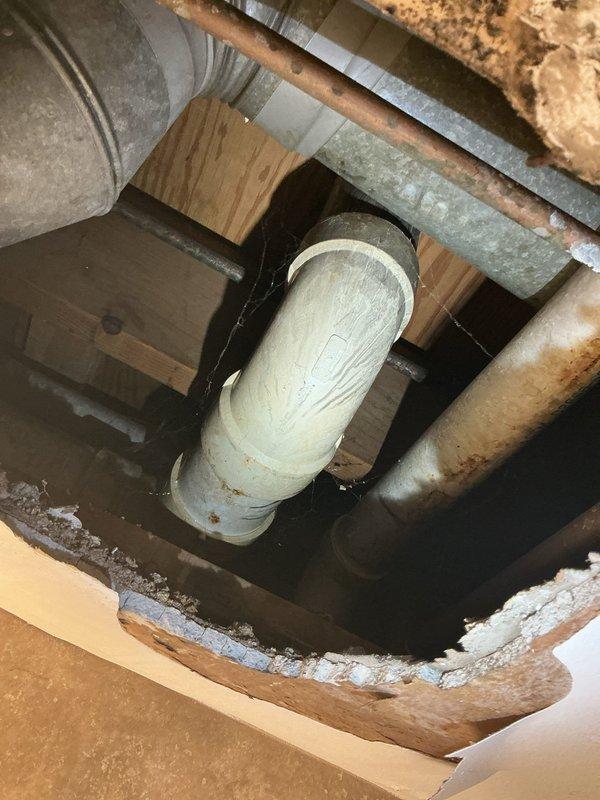 Responded to water leak complaint originating from toilet installation with water penetrating through to basement level. Upon inspection, identified active leak at toilet base with water migrating through floor assembly and draining into basement space below. Photographic documentation revealed water damage and staining on PVC drain pipe and surrounding floor joists in basement ceiling cavity, along with deteriorated condition of floor drain and buildup around toilet mounting area. Diagnosed compromised wax ring seal at toilet flange connection as primary leak source. Removed toilet fixture, replaced failed wax ring seal, inspected toilet flange for damage and proper alignment, reinstalled toilet with new mounting hardware, and verified proper seal. Tested system with multiple flush cycles to confirm leak elimination and proper drainage function.