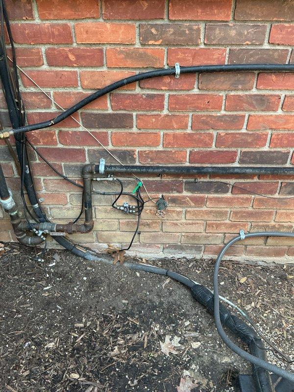 Responded to service call for exterior hose spigot reported as broken by HVAC technician during routine maintenance. Upon inspection, identified damaged exterior faucet assembly mounted to brick wall with compromised connection points and potential for water intrusion. Assessed exterior utility piping system including associated black conduit runs and mounting hardware secured to brick facade. Evaluated interior supply line connections including braided flex line and corrugated feed hose with visible mounting brackets showing signs of age-related deterioration and paint failure on surrounding trim work. Documented existing conditions of both exterior spigot installation and interior plumbing connections to determine appropriate repair recommendations and prevent potential leak damage.