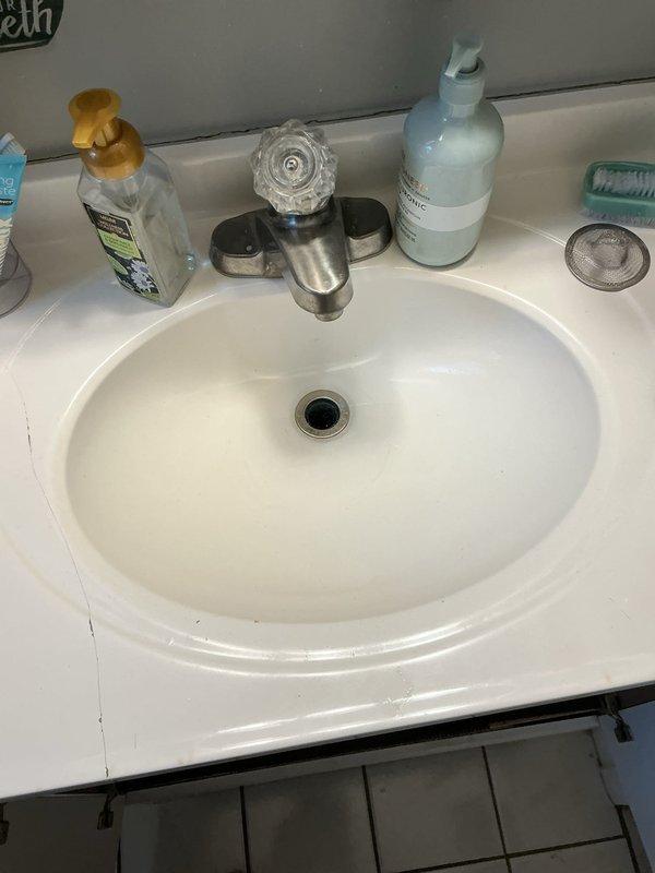 Responded to service call for clogged bathroom sink that had been non-functional for several days. Upon arrival, performed diagnostic inspection of white oval bathroom sink with integrated countertop and standard chrome drain assembly. Assessed visible plumbing components including brushed metal faucet fixture and drain system. Conducted under-sink inspection revealing standard P-trap configuration with white PVC piping and black braided water supply lines connected to faucet assembly. Diagnosed blockage location within drain system. Cleared obstruction from sink drain using appropriate plumbing tools and techniques. Verified proper water flow and drainage function upon completion. Tested P-trap connections for leaks and confirmed all plumbing components were secure and functioning correctly. Sink restored to full operational status.
