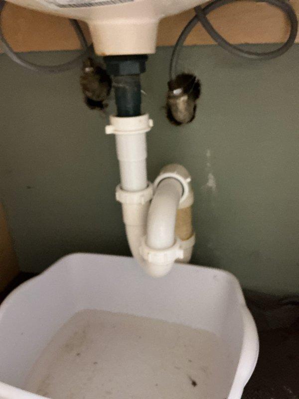 Responded to service call for clogged bathroom sink that had been non-functional for several days. Upon arrival, performed diagnostic inspection of white oval bathroom sink with integrated countertop and standard chrome drain assembly. Assessed visible plumbing components including brushed metal faucet fixture and drain system. Conducted under-sink inspection revealing standard P-trap configuration with white PVC piping and black braided water supply lines connected to faucet assembly. Diagnosed blockage location within drain system. Cleared obstruction from sink drain using appropriate plumbing tools and techniques. Verified proper water flow and drainage function upon completion. Tested P-trap connections for leaks and confirmed all plumbing components were secure and functioning correctly. Sink restored to full operational status.