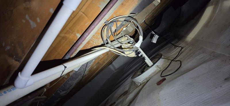 Responded to warranty call for water overflow from coil drain line onto utility room floor. Upon crawl space inspection, found sump pump disconnected with power cord on floor and reconnected pump to ceiling-mounted outlet. Discovered 3/4" PVC condensate drain line improperly secured with zip ties to lineset, creating multiple bows with inadequate pitch preventing proper drainage. Identified that approximately 30 feet of drain line requires either proper pitch correction and routing to sump pump, or installation of condensate pump with shortened 6-foot run to nearby sink for code-compliant drainage.