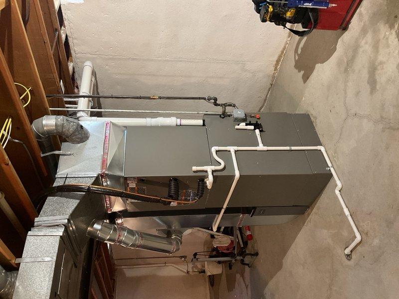 Completed full HVAC system installation including new furnace and air conditioning unit in basement utility area. Installed gray furnace unit with associated white PVC condensate drainage and venting system, along with metal exhaust vent piping properly routed and secured to walls. Connected all ductwork including metallic flex ducts to distribution system. Verified thermostat wiring and programming. Performed system startup, checked all electrical connections, tested airflow at registers, and confirmed proper operation of both heating and cooling modes. Measured system performance and verified equipment meets efficiency requirements for available utility rebate programs. All work performed to code with permit documentation submitted.