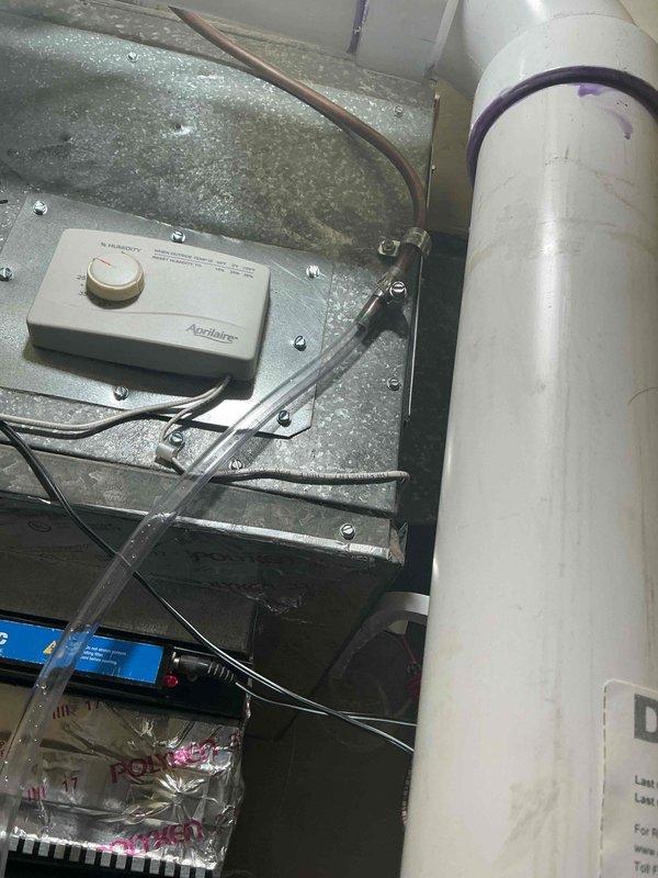 Responded to service call for 8-year-old air conditioning system with evaporator coil located in kitchen area. Performed diagnostic evaluation of condensate drainage system and identified deteriorated vinyl tubing on condensate pump requiring replacement. Assessed copper condensate line condition and recommended blowout service to ensure proper drainage flow. Inspected Aprilaire humidifier control unit and associated mechanical components in attic installation. Documented equipment condition with photos showing condensate pump assembly, PVC drainage piping with shutoff valves, HVAC ductwork, and copper tubing routing. Provided detailed estimate for replacement of vinyl condensate pump drain tubing and copper line service to prevent future water damage and maintain proper system operation.