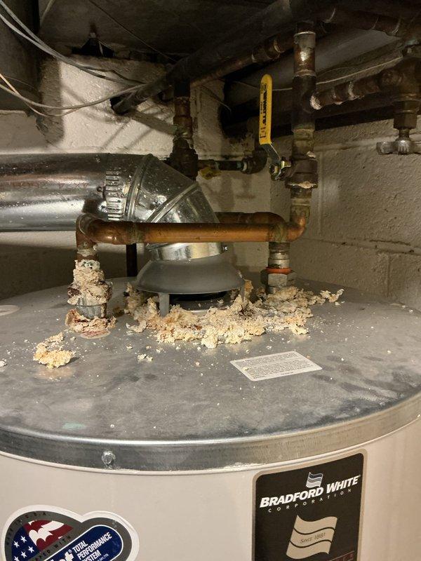 Responded to diagnostic request for Bradford White tanked water heater showing signs of corrosion as noted during previous service visit. Upon inspection, found significant accumulation of deteriorated insulation material and debris on top of unit around pipe connections. Examined copper supply lines and observed age-related oxidation and discoloration. Assessed overall condition of unit including top-mounted connections, piping integrity, and external surfaces for corrosion or deterioration. Documented findings with photographs showing debris accumulation and general equipment condition. Unit remains under full parts and labor warranty coverage.