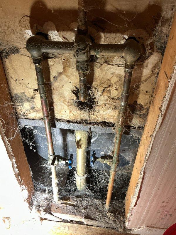 # Bathroom Plumbing Repair and Drain Service

Responded to service call for multiple bathroom plumbing issues including leaking bathtub faucet, broken control knob, and clogged sink drain. Upon inspection, identified deteriorated bathtub fixtures with significant rust staining and water damage along tub-to-wall junction, indicating prolonged moisture exposure.

Accessed concealed plumbing assembly by removing wall cavity access panel, revealing aged copper supply lines with visible corrosion and PVC drain configuration with dual shut-off valves. Addressed clogged sink drain using appropriate clearing methods. Assessed bathtub faucet assembly with three chrome fixtures mounted on tile wall, noting one cross-handle valve required replacement due to mechanical failure. Evaluated extent of rust deterioration at fixture base and tub spout area to determine necessary repairs. Documented existing conditions including compromised sealing at tub-wall interface and aging plumbing infrastructure 
