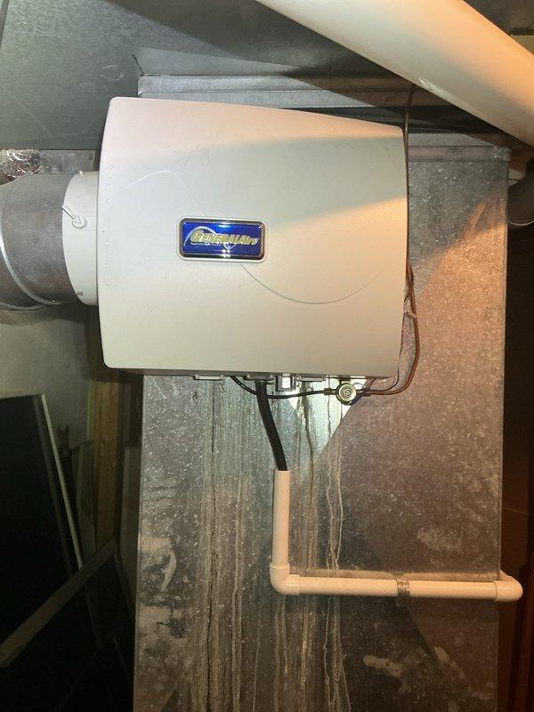 Completed comprehensive Gold AC inspection on 5-year-old residential air conditioning system with air handler located in basement. Verified system operational status and confirmed single-unit configuration. Performed thorough examination of HVAC components including evaporator coil, blower assembly, condensate drainage system, and electrical connections. Inspected integrated humidifier unit mounted to ductwork, verifying proper water supply lines and electrical connections. Evaluated PVC condensate drain piping configuration and checked for proper pitch and drainage flow. Assessed copper refrigerant lines for insulation integrity and signs of wear. Examined ductwork connections and sealed joints. Verified all safety controls, tested thermostat operation, and confirmed adequate airflow throughout system. Documented equipment condition with photographic records showing humidifier installation, mechanical room plumbing configuration, and associated utility connections. System found to be 
