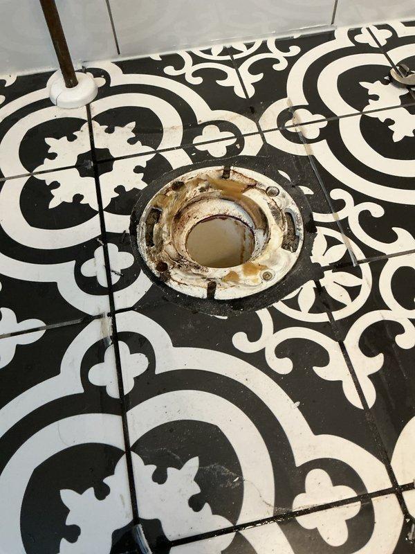 Completed toilet installation with new flange assembly on decorative tile flooring. Removed deteriorated toilet flange showing significant rust staining and water damage, replaced with new white-coated metal drain fixture, and properly secured unit with perimeter screws to ensure watertight seal and stable mounting for toilet reinstallation.