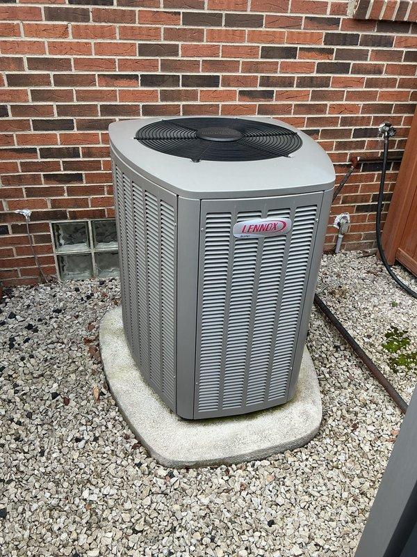 Completed comprehensive Gold-level air conditioning inspection on a 10+ year old Lennox condensing unit located in residential side yard. Unit positioned on concrete pad against brick foundation with air handler/coil assembly located in basement. Performed full system evaluation including visual inspection of outdoor equipment, verification of proper installation clearances, assessment of electrical connections, and examination of refrigerant line sets. Condensing unit found in good overall condition with no visible signs of physical damage, deterioration, or corrosion to cabinet or components. Fan guard and louver panels intact and secure. Concrete pad level and stable with adequate drainage. Refrigerant lines properly insulated and secured along fence line. Documented equipment condition through photographic records for maintenance history files.