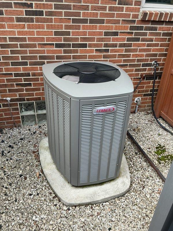 Completed comprehensive Gold-level air conditioning inspection on a 10+ year old Lennox condensing unit located in residential side yard. Unit positioned on concrete pad against brick foundation with air handler/coil assembly located in basement. Performed full system evaluation including visual inspection of outdoor equipment, verification of proper installation clearances, assessment of electrical connections, and examination of refrigerant line sets. Condensing unit found in good overall condition with no visible signs of physical damage, deterioration, or corrosion to cabinet or components. Fan guard and louver panels intact and secure. Concrete pad level and stable with adequate drainage. Refrigerant lines properly insulated and secured along fence line. Documented equipment condition through photographic records for maintenance history files.