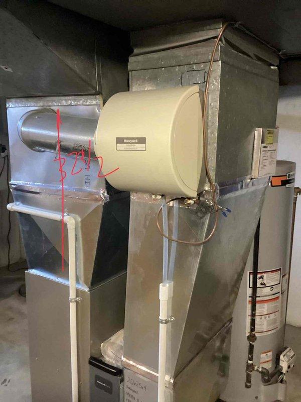 Completed air conditioning tune-up on a 20-year-old AC unit located in the basement. Performed standard maintenance procedures including system inspection, cleaning, and performance verification of the cooling system. The HVAC installation includes a gray metal furnace with mounted Honeywell humidifier, associated ductwork with reflective insulation, and a water heater in the mechanical room area.