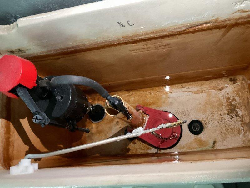 Performed comprehensive whole home plumbing inspection in response to unusually high water consumption. Conducted thorough examination of all plumbing fixtures, supply lines, and drainage systems throughout the property. Inspected toilet tank components and identified significant mineral buildup, rust staining, and corrosion on interior surfaces, indicating prolonged water exposure and possible inefficient flush valve operation. Documented deteriorated flapper valve assembly with red rubber flapper showing signs of wear, potentially causing continuous water seepage into bowl between flushes. Observed fill valve mechanism with blue float ball assembly displaying mineral deposits that could affect proper shutoff function. Noted extensive discoloration and sediment accumulation on tank bottom and walls, suggesting water quality issues and age-related component degradation. Tank components showed evidence of oxidation on metal parts and hardwater scale throughout. Photographed conditions f