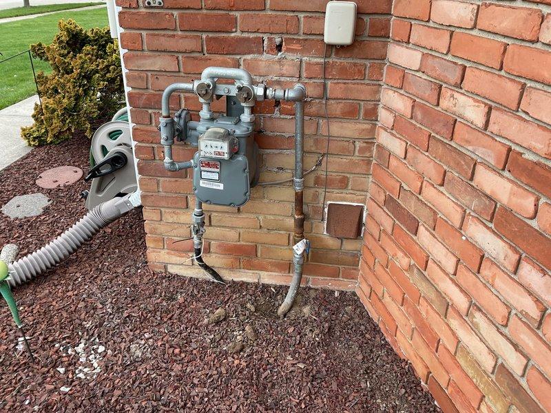 Completed exterior gas line installation and meter setup on residential property. Installed new gray gas meter on red brick exterior wall with proper mounting and multiple metal pipe connections routed vertically and horizontally for functional gas distribution system. Connected galvanized steel piping from meter to building entry points, ensuring secure fittings and proper integration with existing utility infrastructure. All connections tested and verified for safety compliance.