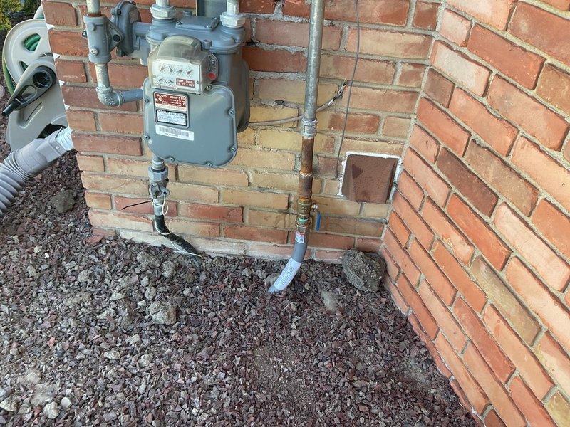 Completed exterior gas line installation and meter setup on residential property. Installed new gray gas meter on red brick exterior wall with proper mounting and multiple metal pipe connections routed vertically and horizontally for functional gas distribution system. Connected galvanized steel piping from meter to building entry points, ensuring secure fittings and proper integration with existing utility infrastructure. All connections tested and verified for safety compliance.