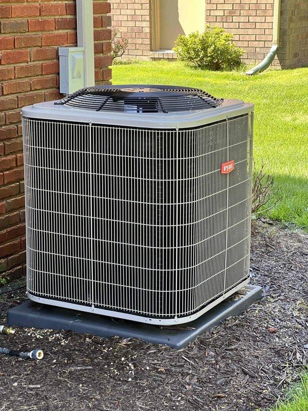 Completed comprehensive Gold Plan AC inspection on 5-year-old residential cooling system with air handler located in basement. Unit found operating properly with condenser positioned on exterior pad against brick wall. Performed standard diagnostic measurements including voltage readings of 295V at disconnect, inspected condenser coil condition, verified fan operation, and checked refrigerant levels. Advised customer to maintain clear area around outdoor unit by removing debris, wood chips, and any animal waste to ensure proper airflow and system efficiency.