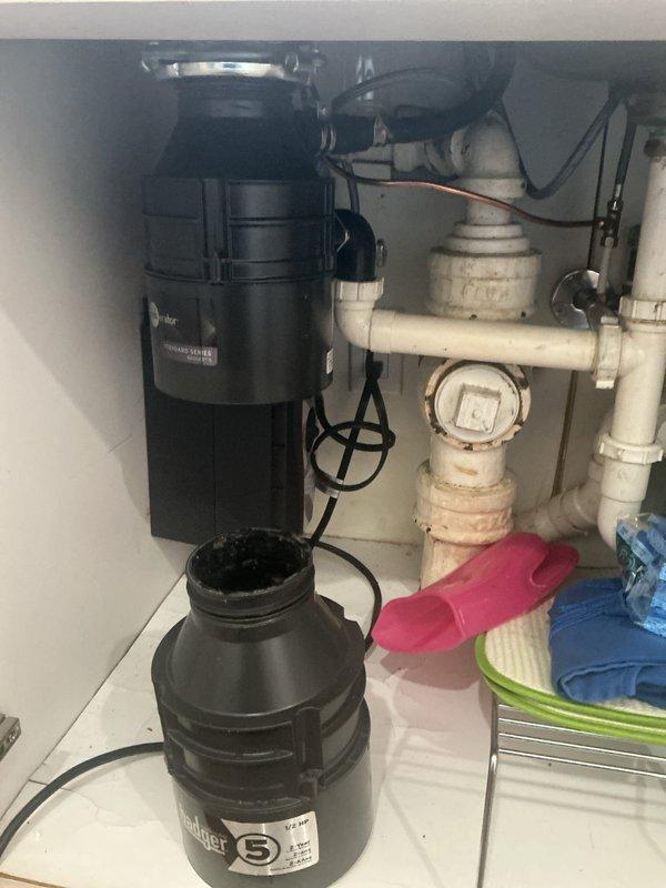 Responded to service call for non-functioning garbage disposal unit. Upon inspection, confirmed that the disposal had never been replaced during the previous October visit when only an estimate was provided. Assessed the existing black InSinkErator garbage disposal unit mounted beneath the kitchen sink, examining electrical connections, mounting assembly, and integration with existing white PVC drain plumbing and P-trap configuration. Documented current under-sink plumbing setup including water filtration system and drainage components for recommendation purposes.