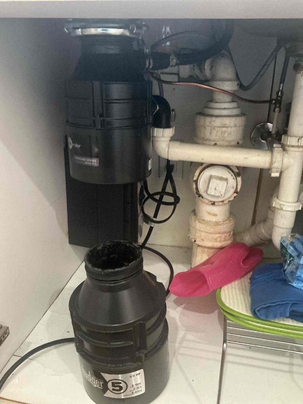 Responded to service call for non-functioning garbage disposal unit. Upon inspection, confirmed that the disposal had never been replaced during the previous October visit when only an estimate was provided. Assessed the existing black InSinkErator garbage disposal unit mounted beneath the kitchen sink, examining electrical connections, mounting assembly, and integration with existing white PVC drain plumbing and P-trap configuration. Documented current under-sink plumbing setup including water filtration system and drainage components for recommendation purposes.