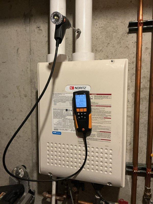 Responded to service call for reported gas odor near 1-year-old furnace located in basement. Upon inspection, identified issue with Noritz tankless water heater exhaust venting system rather than furnace. Performed diagnostic evaluation using combustion analyzer to assess flue gas conditions and verify proper venting. Determined that exhaust vent configuration required modification to meet manufacturer specifications and ensure safe operation. Documented current installation with photos showing existing PVC vent piping and water heater mounting. Identified necessary materials including 3" PVC pipe, fittings, and couplings required to complete vent reconfiguration. Unit is currently operational but requires vent system modifications to address concerns and ensure code compliance.