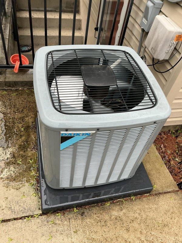 Completed comprehensive Gold AC inspection on single Daikin condensing unit with air handler located on lower level. Performed thorough system evaluation including visual inspection of outdoor condenser unit positioned on concrete pad with proper rubber isolation mounting, verified electrical disconnect box and conduit connections, assessed refrigerant lines, checked fan assembly operation through protective grille, and confirmed adequate clearance around unit perimeter. System found to be in proper working order with no immediate service needs identified; unit under 10 years old and operating within normal parameters.