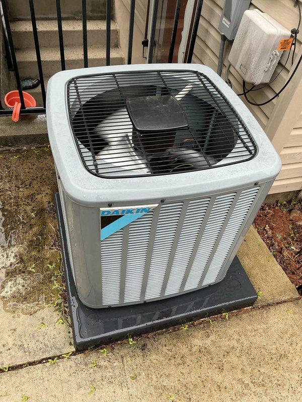 Completed comprehensive Gold AC inspection on single Daikin condensing unit with air handler located on lower level. Performed thorough system evaluation including visual inspection of outdoor condenser unit positioned on concrete pad with proper rubber isolation mounting, verified electrical disconnect box and conduit connections, assessed refrigerant lines, checked fan assembly operation through protective grille, and confirmed adequate clearance around unit perimeter. System found to be in proper working order with no immediate service needs identified; unit under 10 years old and operating within normal parameters.