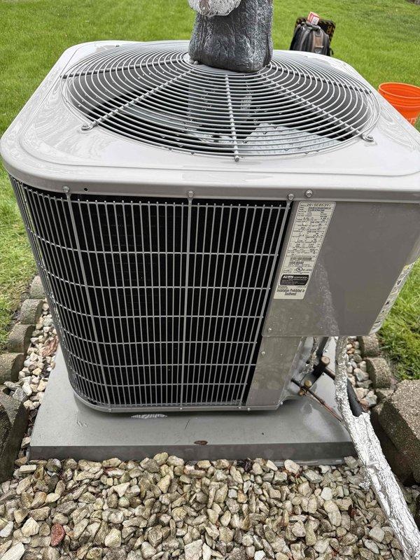 Completed comprehensive Gold AC inspection on 10-year-old residential cooling system with air handler located in basement. Performed standard diagnostic testing and visual examination of outdoor condenser unit and associated components. Documented ambient temperature reading of 56.3°F at time of inspection. Observed condenser unit positioned on concrete pad with decorative stone surround; noted presence of garden ornament on top of unit and advised customer that area surrounding condenser should be kept clear of debris and any animal waste to ensure proper airflow and system efficiency. Verified electrical disconnect box installation and refrigerant line routing. System operational at time of inspection with all components functioning within normal parameters.