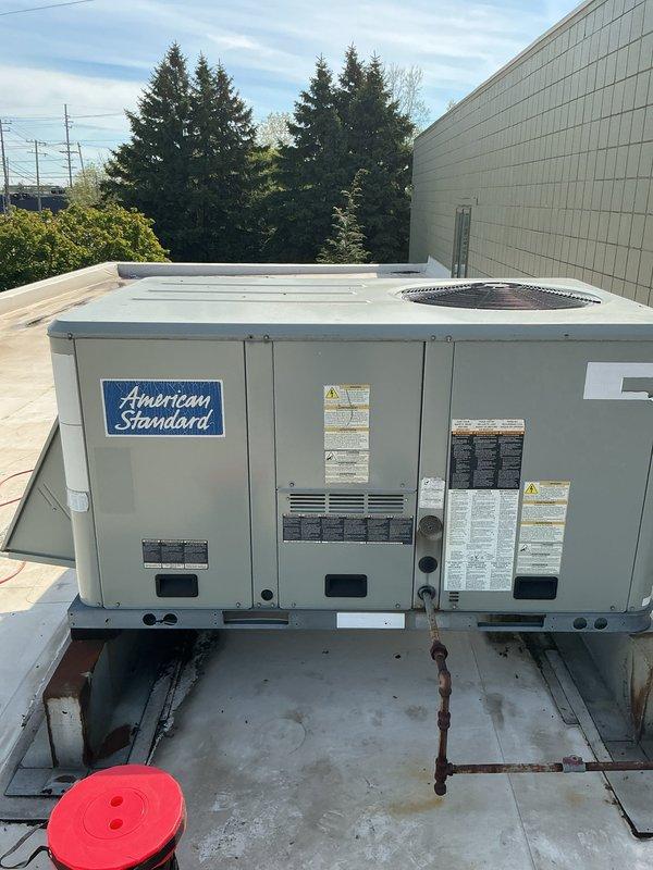 Completed commercial tune-up and inspection on two air conditioning units at commercial facility operating 7:00 AM to 3:30 PM. Accessed rooftop-mounted American Standard packaged heating and cooling system and performed comprehensive preventive maintenance inspection. Verified system operational status and confirmed heating/cooling functions working properly. Conducted electrical diagnostics using HVAC clamp meter, recording voltage and amperage readings to verify proper electrical performance. Measured capacitor values showing 772 microfarads within acceptable range. Inspected all accessible components including compressor, condenser coils, electrical connections, and control systems. Verified unit security and mounting hardware including stabilization chain. Both units found operational with no immediate service needs identified. All safety labels and manufacturer specifications confirmed present and legible.