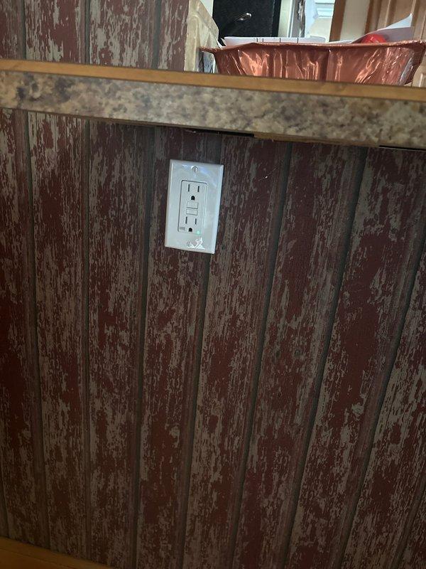 Completed electrical outlet installation and repair in kitchen area with distressed wood paneling. Relocated and secured outlet box to meet code requirements, ensuring proper grounding and connection integrity. Addressed wall deterioration issues around thermostat/control device mounting area, secured electrical components, and verified all connections were functioning safely despite compromised wall conditions.