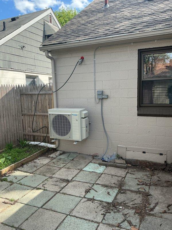 Completed three-day installation of Daikin three-head mini-split system at residential property. Mounted exterior condenser unit on white concrete block wall with refrigerant lines and electrical conduit run along exterior surface to disconnect box near roofline. Installed indoor air handler units in multiple rooms with proper wall mounting and connection to outdoor unit. Ran new dedicated electrical circuit to support system requirements. Obtained mechanical and electrical permits prior to installation. System tested and operational upon completion.