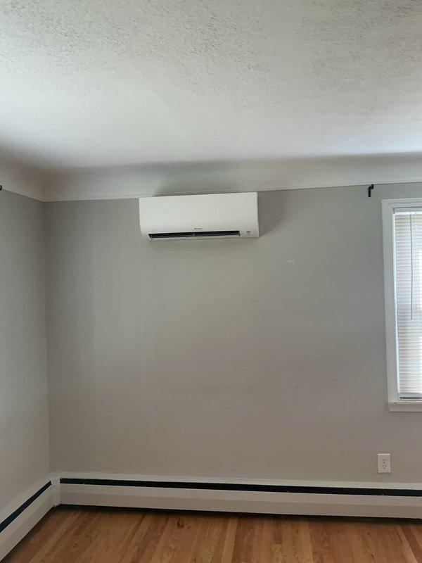 Completed three-day installation of Daikin three-head mini-split system at residential property. Mounted exterior condenser unit on white concrete block wall with refrigerant lines and electrical conduit run along exterior surface to disconnect box near roofline. Installed indoor air handler units in multiple rooms with proper wall mounting and connection to outdoor unit. Ran new dedicated electrical circuit to support system requirements. Obtained mechanical and electrical permits prior to installation. System tested and operational upon completion.