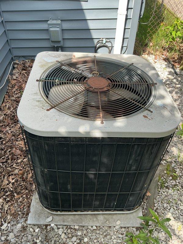 Completed comprehensive Gold AC inspection on residential outdoor condensing unit of unknown age. Unit located on concrete pad with gravel base alongside home exterior. Performed full system evaluation including visual inspection of condenser cabinet, fan assembly, and overall equipment condition. Notable findings include significant rust deterioration on top-mounted fan guard grille and accumulated debris on unit surfaces. Condenser coil grilles show weathering consistent with extended outdoor exposure. Unit operational at time of inspection. Documented equipment condition through photographic records showing dark green/black mesh side panels, rusted fan guard components, and general dirt accumulation. Electrical connections and meter box location noted during external assessment. Equipment exhibits age-related wear patterns requiring monitoring for continued reliable operation.