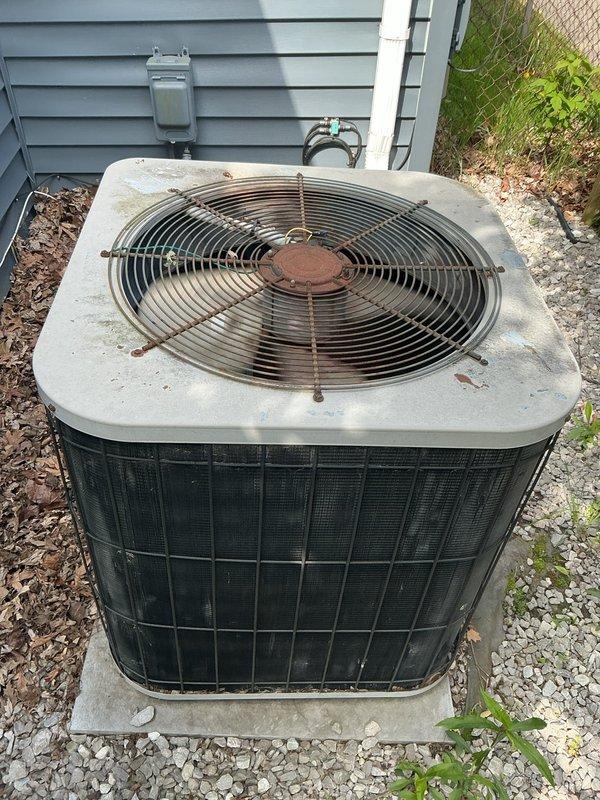 Completed comprehensive Gold AC inspection on residential outdoor condensing unit of unknown age. Unit located on concrete pad with gravel base alongside home exterior. Performed full system evaluation including visual inspection of condenser cabinet, fan assembly, and overall equipment condition. Notable findings include significant rust deterioration on top-mounted fan guard grille and accumulated debris on unit surfaces. Condenser coil grilles show weathering consistent with extended outdoor exposure. Unit operational at time of inspection. Documented equipment condition through photographic records showing dark green/black mesh side panels, rusted fan guard components, and general dirt accumulation. Electrical connections and meter box location noted during external assessment. Equipment exhibits age-related wear patterns requiring monitoring for continued reliable operation.