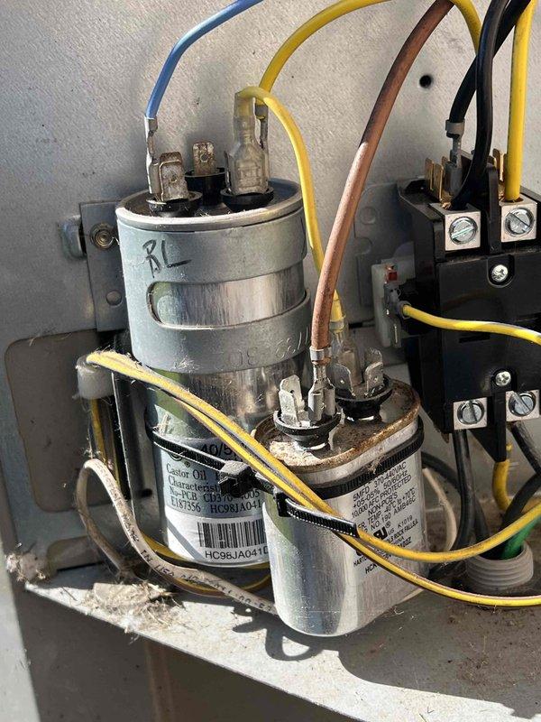 Completed comprehensive Gold AC inspection on 13-year-old residential HVAC system with furnace located in basement. Performed thorough evaluation of outdoor condenser unit positioned on isolation pad against exterior brick wall, inspecting cylindrical unit with vertical grille fins and top-mounted fan assembly. Verified proper operation of all electrical components including dual run capacitor assembly, contactor relay unit, and associated wiring connections with multiple colored conductors. Inspected refrigerant line set routing along exterior wall to disconnect box penetration point. All electrical terminals, spade connectors, and control circuits examined for proper connections and signs of wear. System operating within normal parameters with no immediate service needs identified. Documented equipment condition through photographic records showing capacitor assembly, contactor unit, and exterior condenser placement. Unit showing age-appropriate wear with minor dust accumulation on e